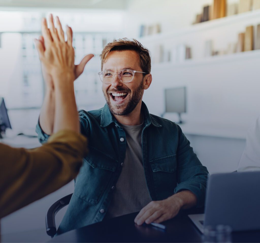 Young man high fiving coworker at an office desk